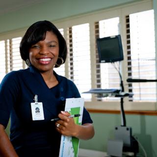 A healthcare professional smiling while holding a clipboard in a medical office.