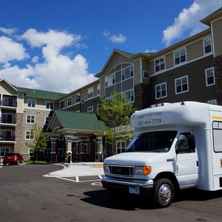 A shuttle van parked in front of a large apartment complex on a sunny day.