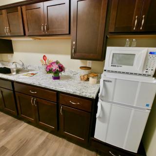 A cozy kitchen with dark wooden cabinets, a countertop adorned with flowers, and essential appliances like a microwave and refrigerator.