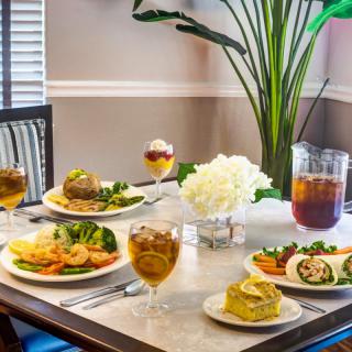 A beautifully set dining table with various dishes and glasses of iced tea, adorned with a white floral arrangement.