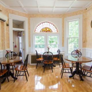A cozy dining area with several tables and chairs, featuring large windows that let in natural light.