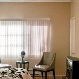 A cozy bedroom with two chairs, a small table, and a window with sheer curtains.