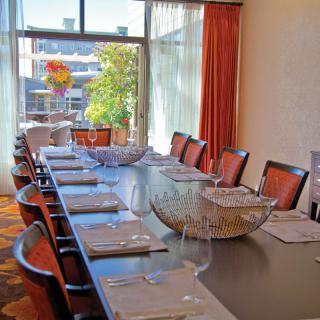 A well-set dining table in a bright room with large windows and orange curtains.