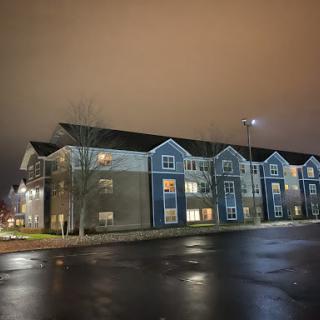 A modern apartment building illuminated at night with a wet street reflecting light.