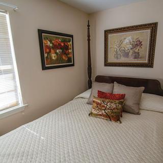 A cozy bedroom with wall art and decorative pillows, illuminated by natural light.