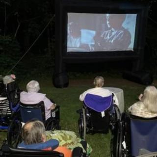 Seniors in wheelchairs enjoying an outdoor movie night under the stars.
