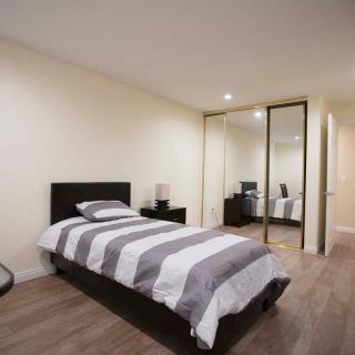 A minimalist bedroom featuring a single bed with striped bedding, a nightstand, and a mirrored closet door.