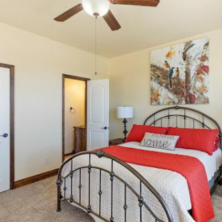 A cozy bedroom featuring a double bed with a vibrant red and white bedding set, complemented by decorative artwork and a ceiling fan.