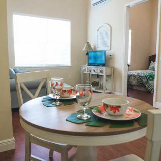 A cozy open-plan dining and living area with a set dining table, featuring floral crockery and glassware.