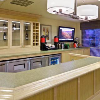 A cozy kitchen and bar area featuring a countertop, cabinets, a coffee station, and a wall-mounted television.