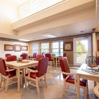 A spacious dining room with red upholstered chairs and wooden tables, well-lit by natural light streaming through large windows.