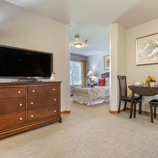 A cozy living space featuring a dresser with a television, leading into a bedroom with a bed and window.