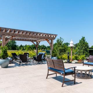 A spacious outdoor patio with a pergola and seating area, surrounded by lush greenery.