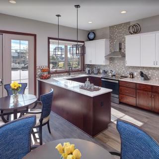 A modern kitchen with a central island and adjacent dining area, featuring pendant lighting and sleek cabinetry.