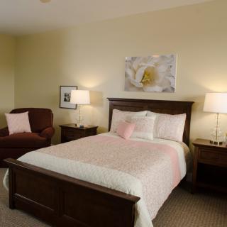 A cozy bedroom with a bed, two lamps, and an armchair.