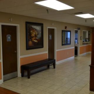 A clinic waiting area with a bench, artwork on the wall, and several doors leading to different rooms.
