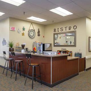 The image depicts a cozy bistro interior with a counter and bar stools, featuring decorative elements and a coffee machine.