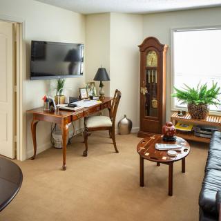 A cozy living room with a desk, grandfather clock, and leather sofa.