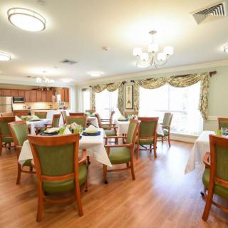 A well-lit dining room with elegantly set tables and chairs, featuring a chandelier and wooden flooring.