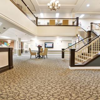 A spacious and elegantly decorated lobby with a carpeted floor, chandelier, and staircase.