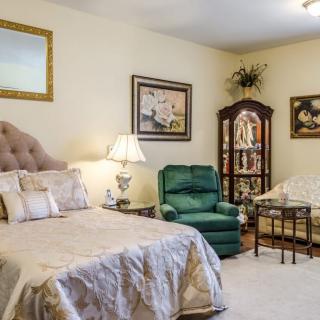 A cozy bedroom with elegant furnishings, including a bed, armchair, and decorative cabinet.