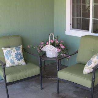 A cozy patio setup with two green cushioned chairs and a small table adorned with a basket of flowers.
