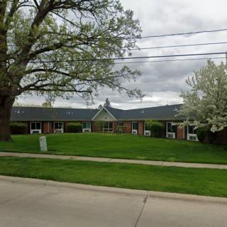 A suburban building surrounded by trees and a well-maintained lawn on a cloudy day.