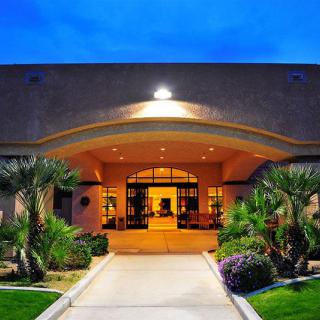 A hotel entrance warmly lit at nighttime, featuring palm trees and well-maintained landscaping.