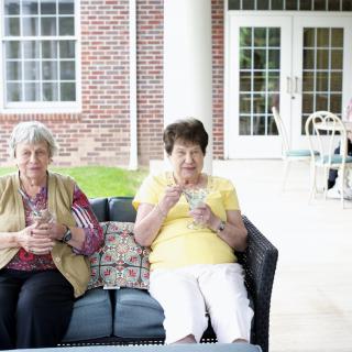 Two elderly women sitting on a porch, enjoying their time outdoors.