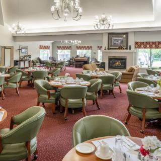 A spacious dining area with multiple tables and chairs, featuring elegant chandeliers and a cozy fireplace.