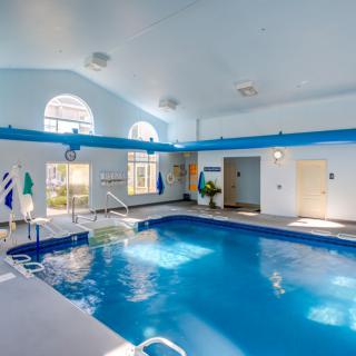 A well-lit indoor swimming pool area with large windows and clean, blue water.