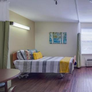 A well-lit hospital room with a neatly made bed, curtains, and a window.