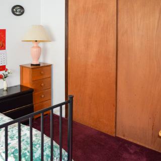 A cozy bedroom with a bed, dresser, and closet featuring a bedside lamp and calendar on the wall.