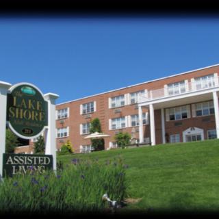 A sunny day view of an assisted living facility with a sign and landscaped front yard.