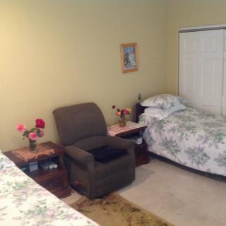 A cozy bedroom with twin beds, a comfortable chair, and a small table with flowers.