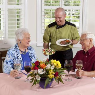 An elderly couple is being served a meal by a waiter in a restaurant setting.