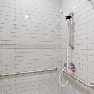 An accessible bathroom shower with white tiles, grab bars, and a handheld showerhead.