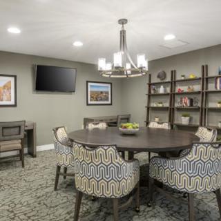 A modern conference room with a round table, patterned chairs, a chandelier, bookshelves, and wall-mounted television.