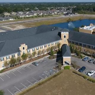 Aerial view of a large building with adjacent parking lot and nearby water body in a suburban area.