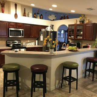 A cozy kitchen with a curved countertop and bar stools, featuring wooden cabinets and modern appliances.