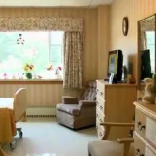 A cozy room with wooden furniture and a large window, typical of a nursing home setting.