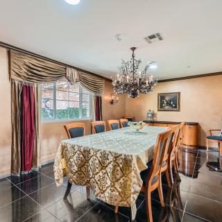 A well-appointed dining room featuring a large table with elegant chairs, illuminated by a chandelier and enhanced by decorative curtains and artwork.
