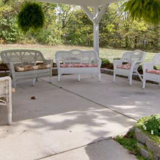 A cozy outdoor patio with wicker furniture and lush greenery under a gazebo.