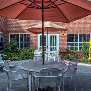A cozy outdoor patio with tables, chairs, and umbrellas set against a brick building.