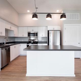 A modern kitchen with white cabinets, stainless steel appliances, and a central island with overhead lighting.