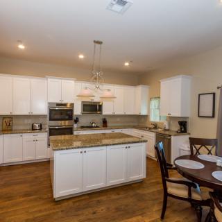 A modern kitchen with white cabinets, a central island, and wooden flooring, featuring a small dining table.