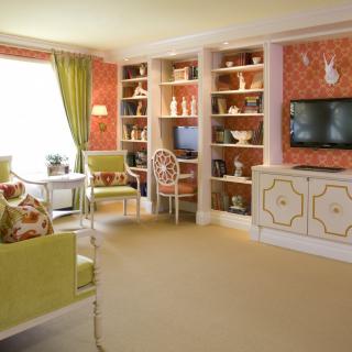 A vibrant living room featuring colorful decor, green accents, and a cozy seating area with shelves and a television.