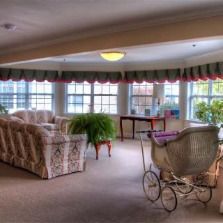A vintage-style living room with floral patterned furniture, large windows providing natural light, and decorative plants.