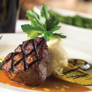 A gourmet dish featuring grilled steak with mashed potatoes and garnished with herbs.