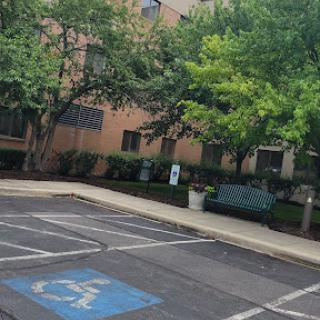 A view of an empty parking lot featuring a designated handicap space and a building surrounded by trees.